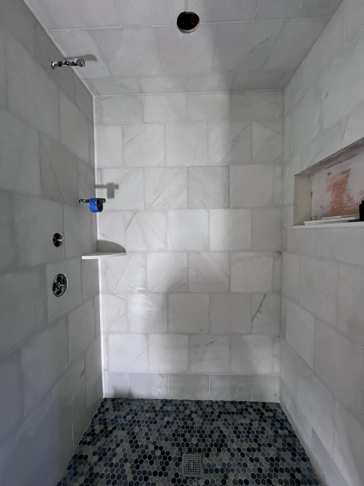 Finished marble-tile shower with dark hexagonal mosaic floor